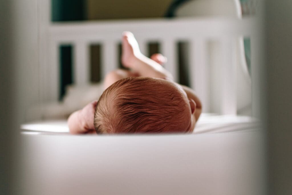 Baby is laying on a light pink sheet in crib. Shot is taken from top of babies head and you can see their newborn hair and legs sticking up.